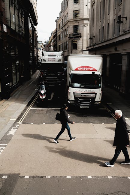 A street scene showing two white delivery trucks parked close together, one labeled 'Uniserve' with a website address, and the other with the branding 'Bexon Transport,' positioned on a narrow urban r